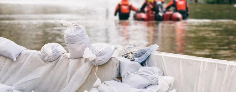 close-up of white sandbags holding back flood water with rescuers in a lifeboat in the background