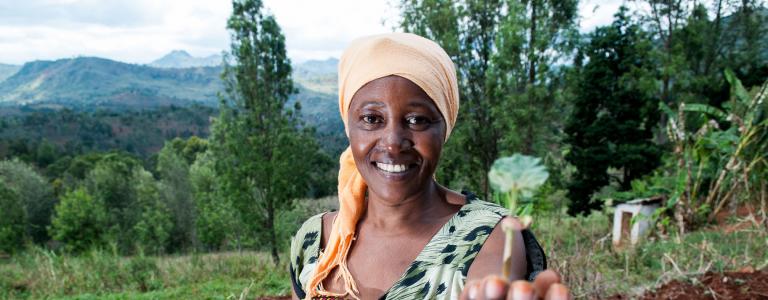 A smiling women in a field holding a flower 