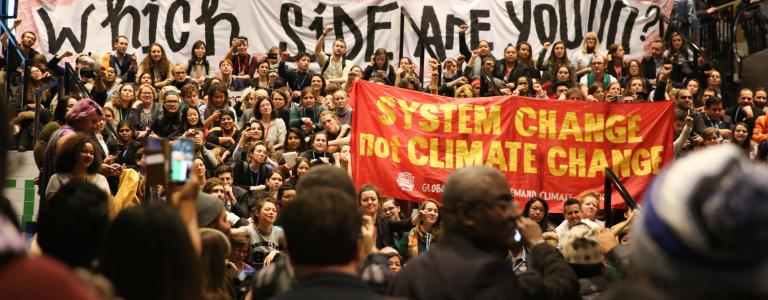 A crowd of activists at COP 24 holding a sign reading "Which side are you on?"