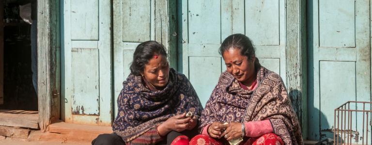 Two older women from Nepal sit on a step in the sun