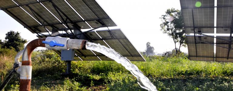 Water tap behind solar panels in a field.