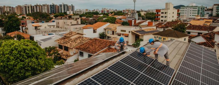 Workers install solar panels on a roof with a city set behind.