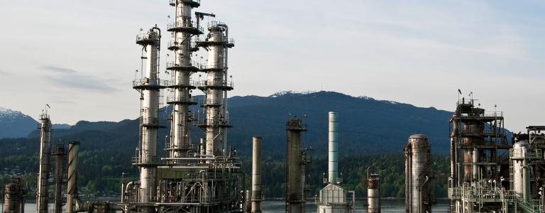 Oil refinery with river and forested mountain in the background.