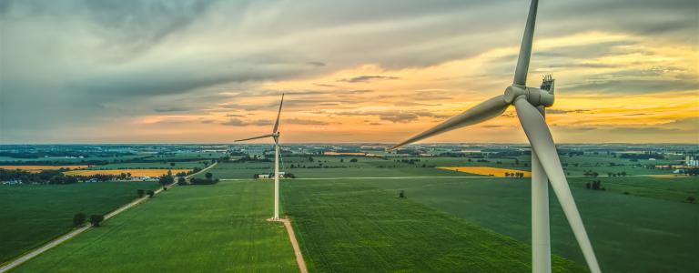An aerial image of two wind turbines in rural farmland at sunset in Southwestern Ontario, Canada