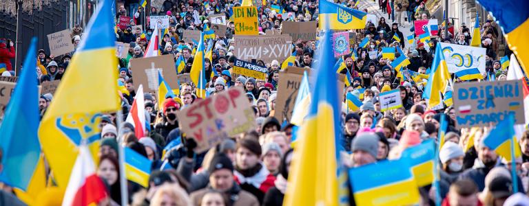 A street full of people march with flags in support of Ukraine.