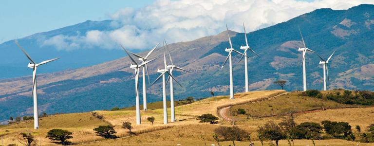 Wind turbines stand in front of a mountain landscape in Costa Rica.