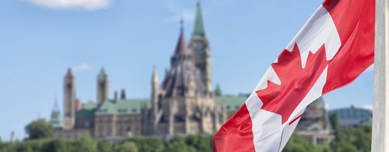 A Canada flag flies with the parliament buildings set in the background.
