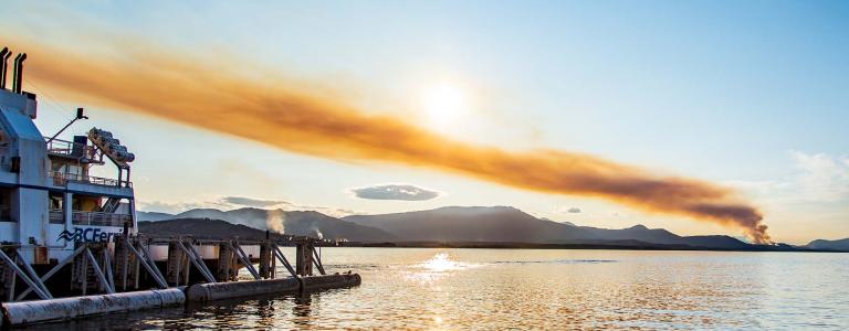Smoke from a distant bush fire near Ladysmith, British Columbia is seen from Vesuvius Bay. A ferry is seen on the left.