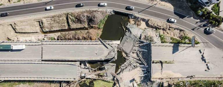 Two bridges appear destroyed while a third allows cars to cross a river.
