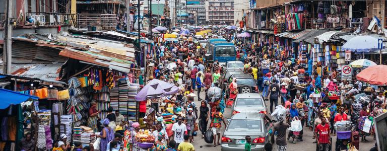 City residents and vehicles flood a street market in Nigeria.