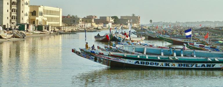 Boats rest on the water near city buildings in Senegal. Photo: Unsplash / E. Diop
