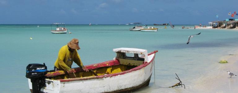 A fisherman standing in the water with his small boat.