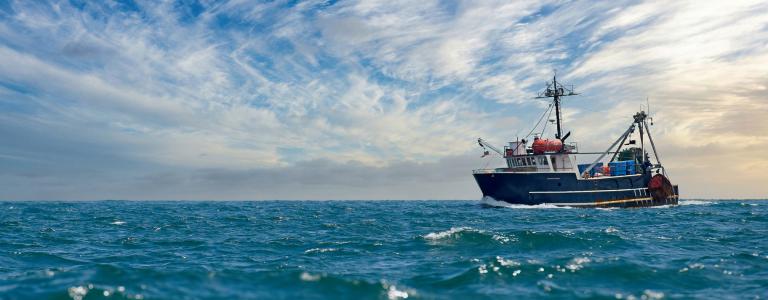 A lobster fishing boat sails across the ocean under a blue but cloudy sky.