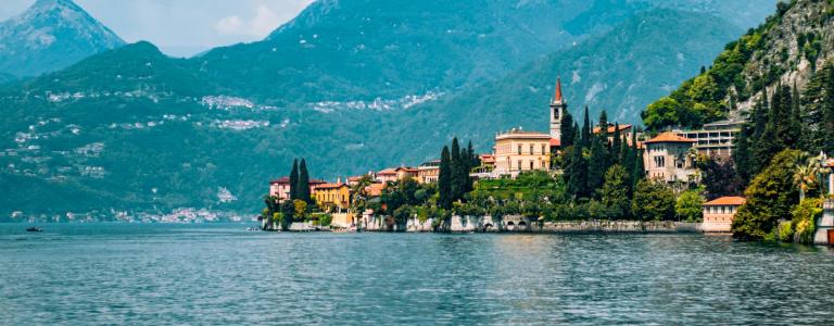 Buildings near a lake surrounded by mountains on a sunny day.