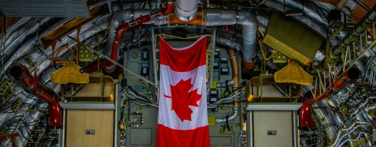 Canadian flag hanging in the middle of a factory with pipes surrounding it. 