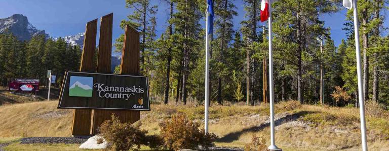 Kananaskis county sign stands beside a road way with flags standing to the side.