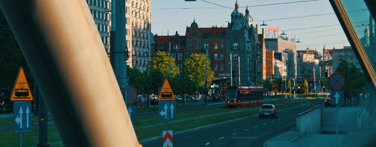 City view with a tram and car, buildings in the background.