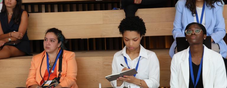 Three young women sit on the steps of an auditorium