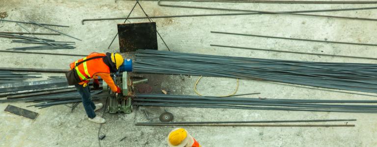 People in protective gear at a construction site loading steel rods.