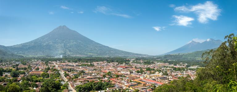 Landscape of a city in Guatemala surrounded by nature. There are mountains and a volcano in the background.