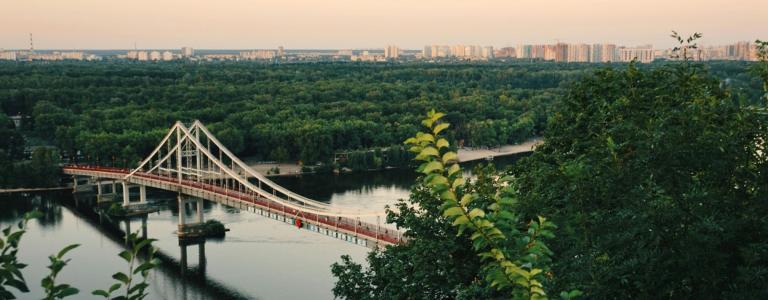 A bridge runs over a river, with the city of Kyiv in the background.