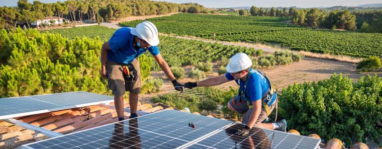 Two workers attach solar panels to a roof