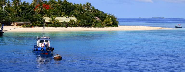 Blue fishing boat in the sea near a white sand beach in Fiji.