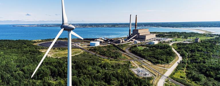 A wind turbine stands in front of a coal plant