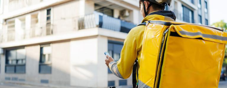 A delivery driver on a bicycle uses a smartphone to navigate the city.