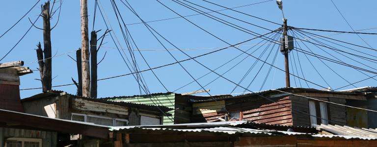 A web of electric cables runs from a street light pole to shacks.