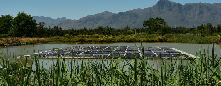 Solar panels floating on a pond with grasses in the foreground and mountains behind.