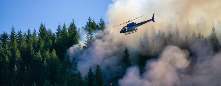 A helicopter flies near fire smoke in the Rocky Mountains.