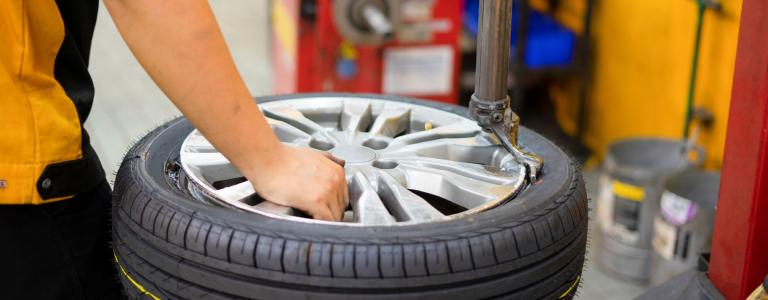 Person working in a body shop filling up a tire at a table.