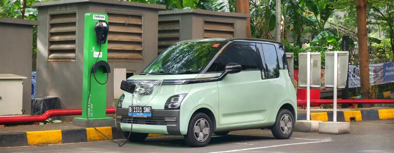Electric wuling car charging at EV charging station with lush tropical greenery in the background.