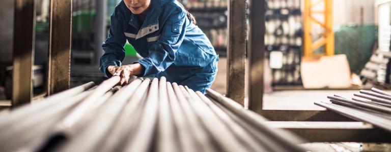 Female factory worker lays steel pipes in full protective gear.