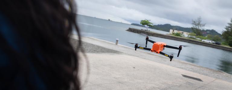 A small, orange drone flies low to the ground on a pier.