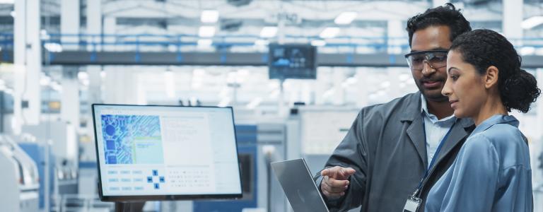 A man and a woman look at a laptop in a factory.