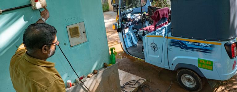A person charges an electric 3-wheeler.