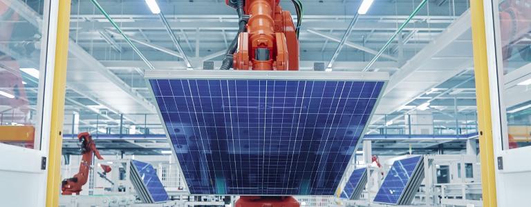 A mechanical arm in a factory lifting a solar panel