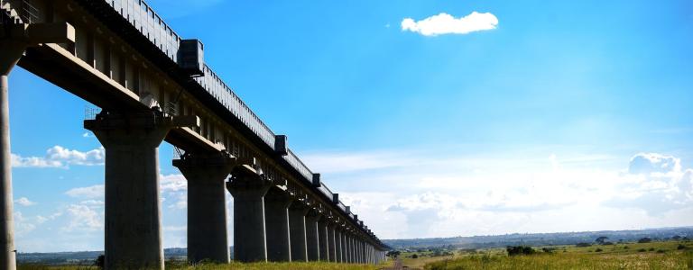 Railway tracks raised off the ground alongside a dirt track in Kenya.