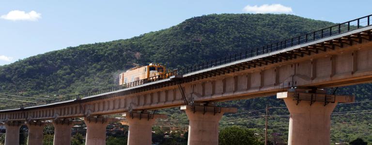 Yellow train on a standard railway bridge along the Mombasa Nairobi transport industry route, moving across Kenya. Also known as the Madaraka Express.