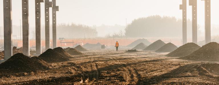 A worker is seen walking under a massive frame at a construction site.