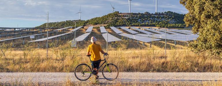 Person with a bike stands in front of solar panels and wind mills