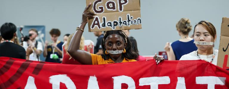 Civil society demonstrators at UNFCCC COP 30 hold signs reading, "global adaptation gap."