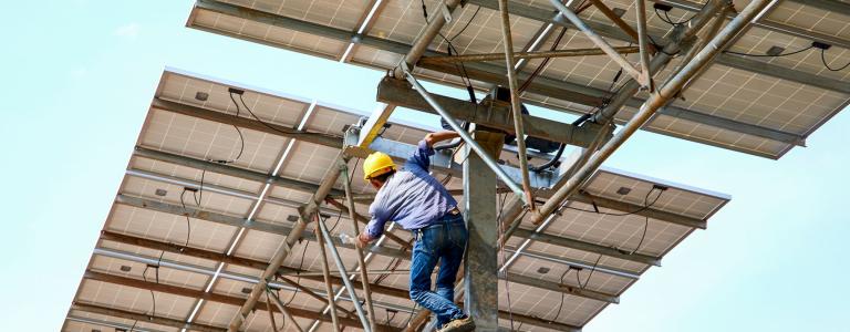 A worker in a hardhat stands below two solar panels.