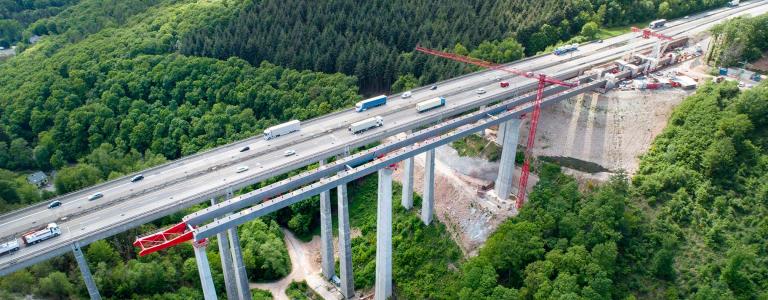 Construction site of a highway bridge over a valley with vehicles driving. 