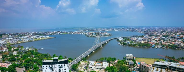 A bridge crosses a aide river in the middle of a green city