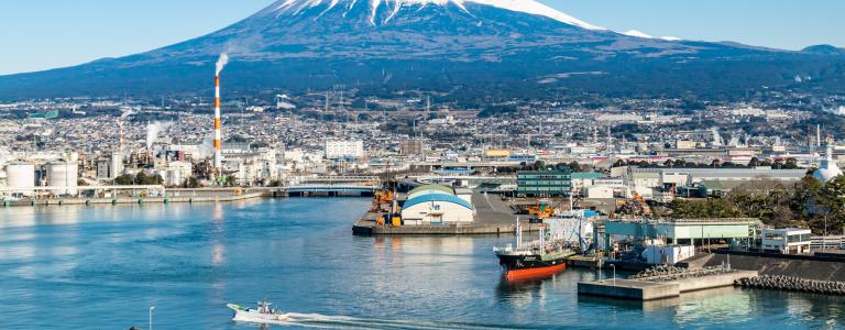 A shipping port in a city's industrial area, with a mountain in the background.