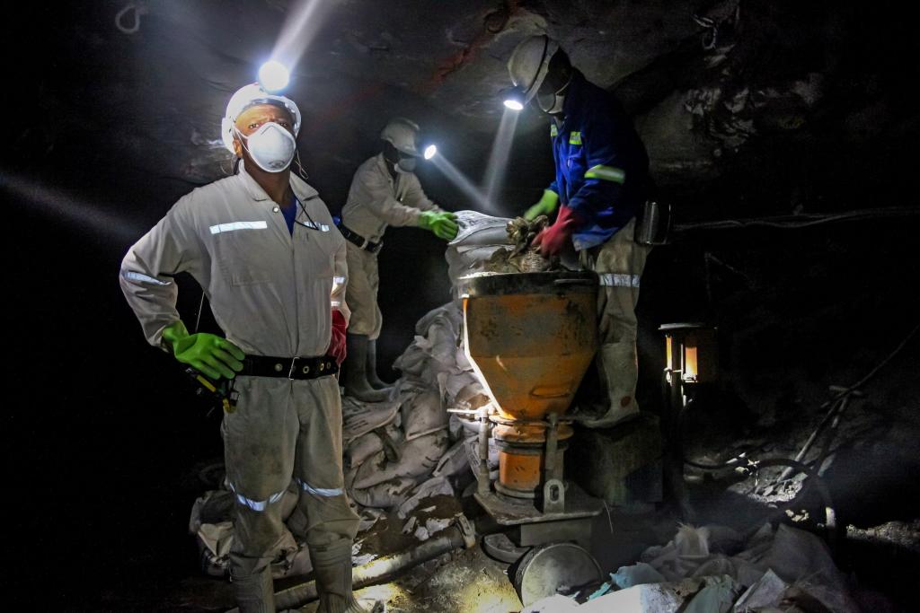 Miners mix cement with headlamps on while underground in a dark platinum mine