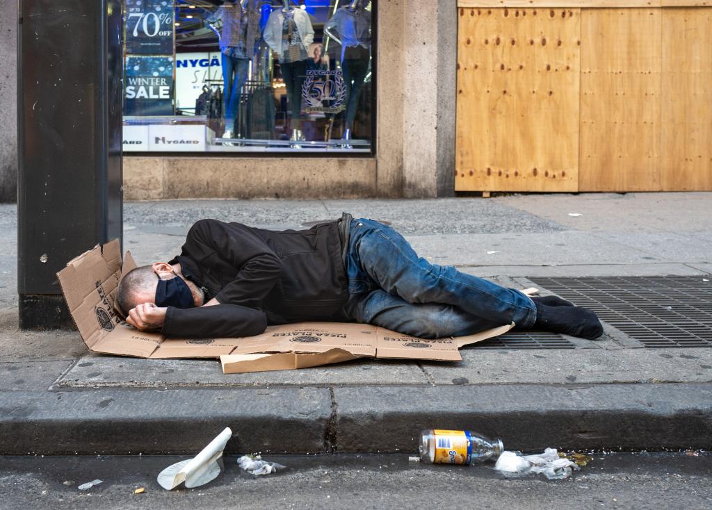 A man in a face mask sleeps on cardboard in New York